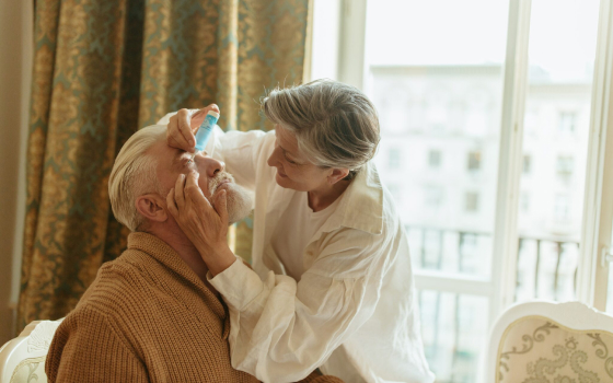 Woman administering eye drops to man.