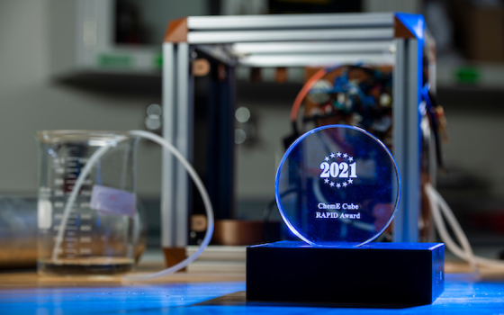 Image of the 2021 ChemE Cube RAPID Award in front of the winning ChemE Cube from the S&T team.