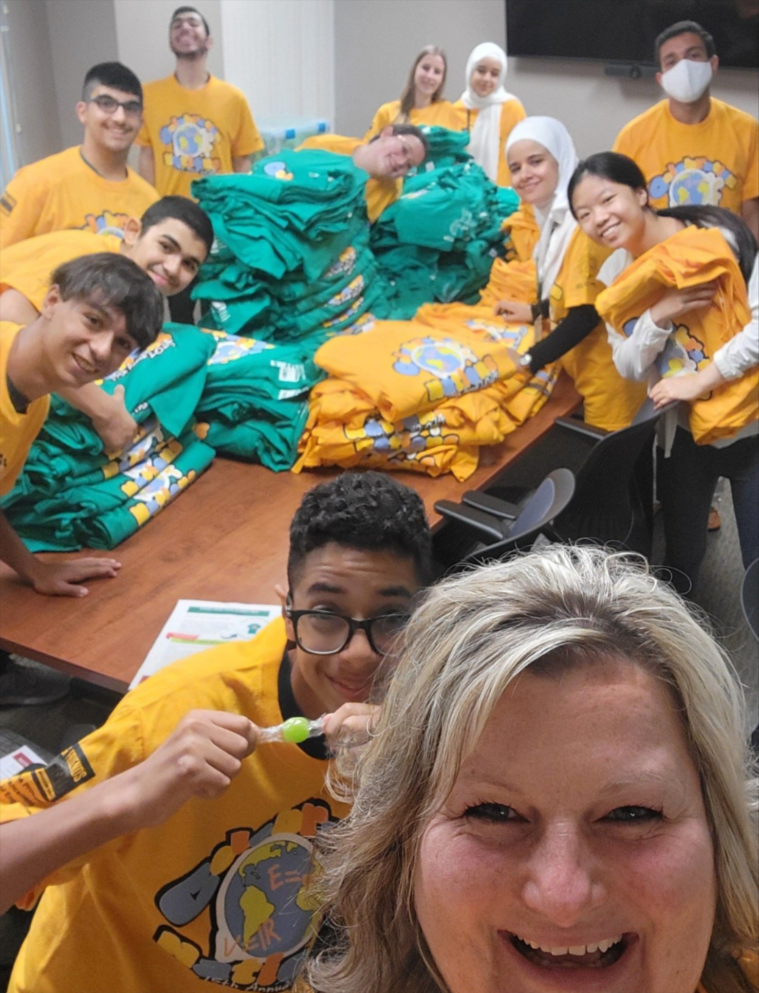 Multiple people posing for the camera while sporting Celebration Of Nations T-shirts, and they are folding the shirts for the event.