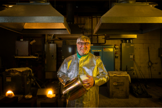 Dr. Ron O’Malley smiling in the foundry with a lab coat and goggles on