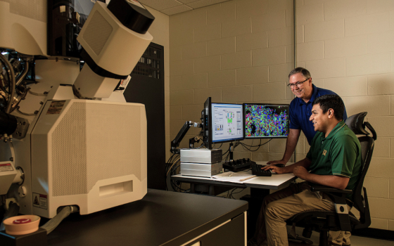 Image of Joe Newkirk and Cesar Ortiz collaborating analyzing research at a computer with three monitors