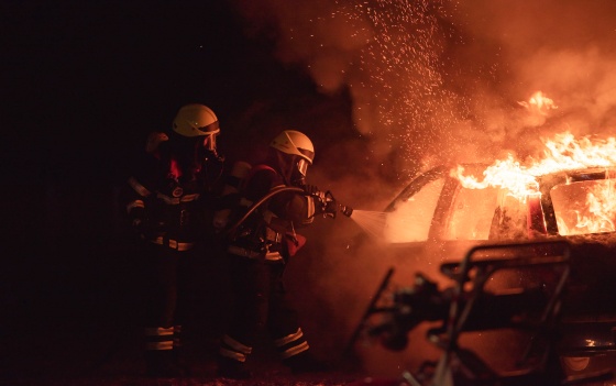 Photo of two firemen putting out a car fire with a hose