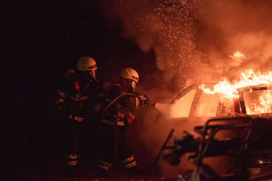 Photo of two firemen putting out a car far